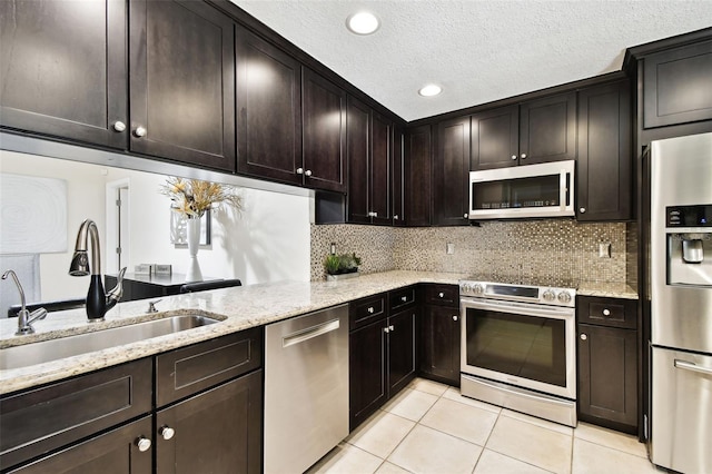 kitchen with tasteful backsplash, a sink, light stone counters, stainless steel appliances, and light tile patterned flooring