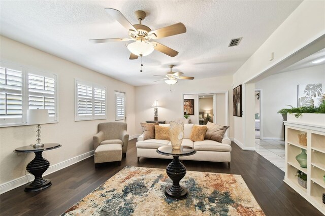 living room featuring a textured ceiling, a ceiling fan, baseboards, dark wood-type flooring, and visible vents