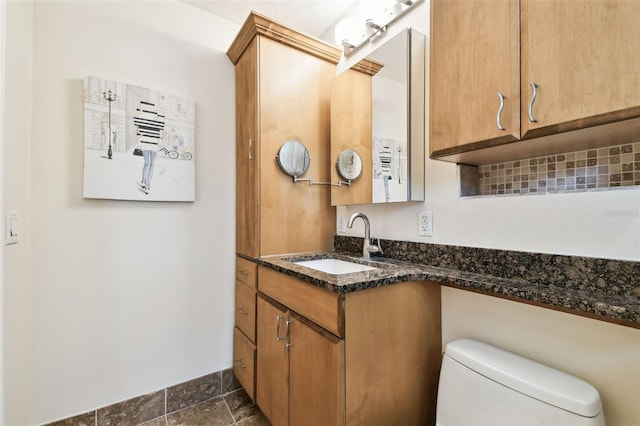 bathroom with toilet, stone finish flooring, and vanity