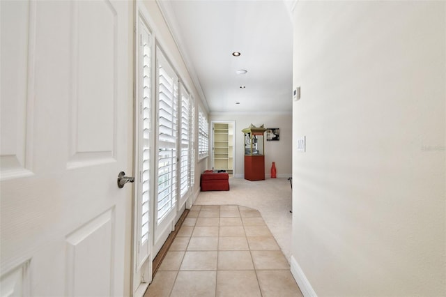hallway featuring light tile patterned floors, baseboards, ornamental molding, and light colored carpet