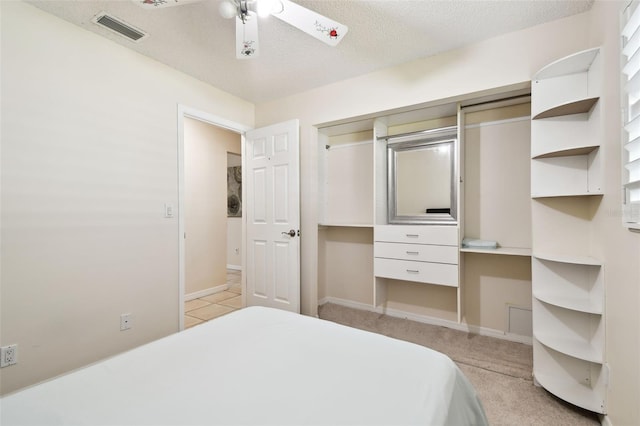 bedroom with ceiling fan, light carpet, a textured ceiling, baseboards, and visible vents