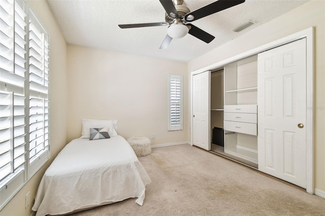 bedroom with multiple windows, light carpet, a textured ceiling, and visible vents