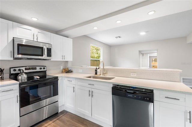 kitchen featuring a peninsula, appliances with stainless steel finishes, dark wood-style flooring, light countertops, and a sink