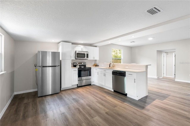 kitchen with a peninsula, white cabinets, visible vents, appliances with stainless steel finishes, and a sink