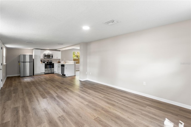 unfurnished living room featuring visible vents, baseboards, a sink, a textured ceiling, and wood finished floors