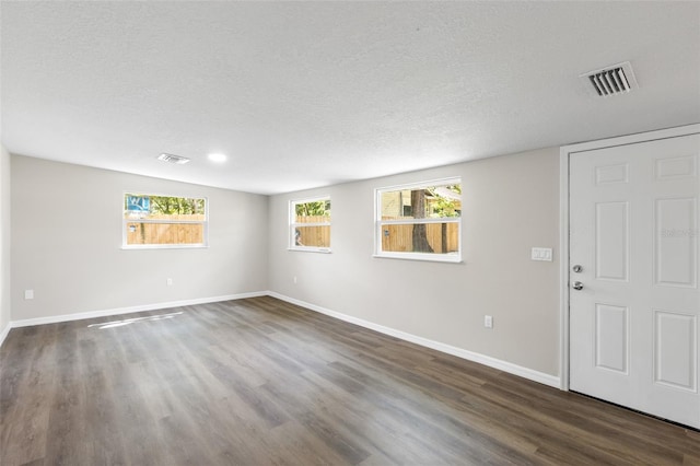 interior space featuring a textured ceiling, dark wood-style flooring, baseboards, and visible vents