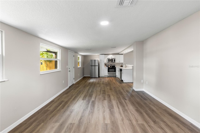 unfurnished living room with a textured ceiling, visible vents, dark wood-style flooring, a sink, and baseboards