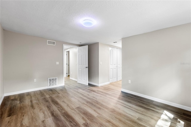 unfurnished room featuring visible vents, baseboards, wood finished floors, and a textured ceiling