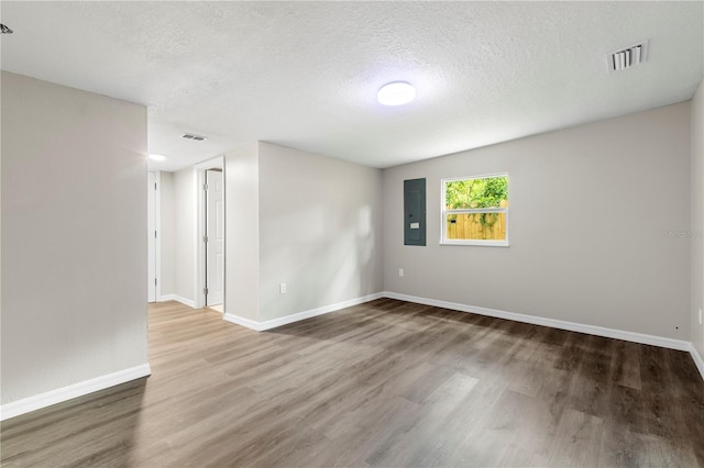 spare room with electric panel, visible vents, baseboards, and wood finished floors