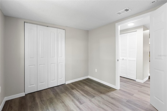 unfurnished bedroom with visible vents, baseboards, a closet, and wood finished floors