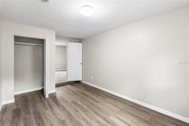 unfurnished bedroom featuring a closet, baseboards, wood finished floors, and a textured ceiling