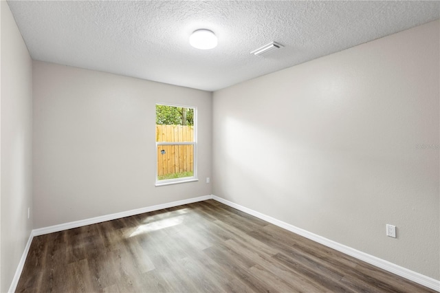 unfurnished room with visible vents, baseboards, a textured ceiling, and wood finished floors