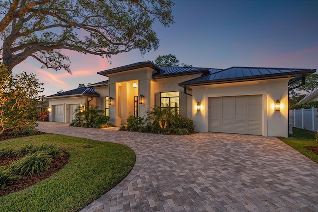 prairie-style home featuring a garage, stucco siding, a standing seam roof, and decorative driveway