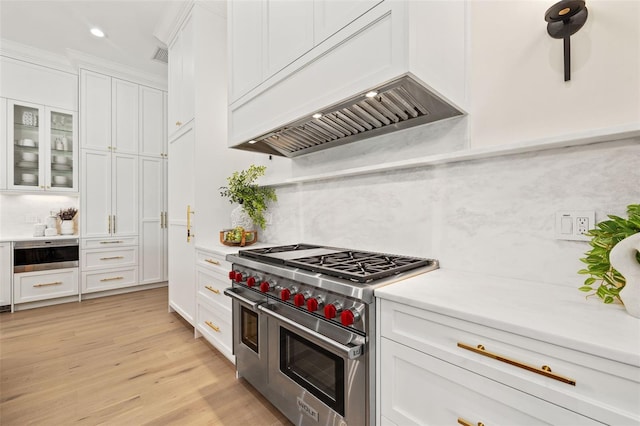 kitchen featuring custom exhaust hood, backsplash, range with two ovens, and white cabinets