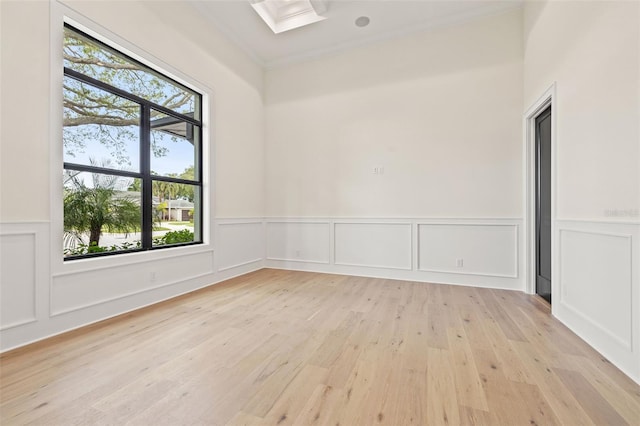 spare room featuring a skylight, light wood finished floors, crown molding, and wainscoting