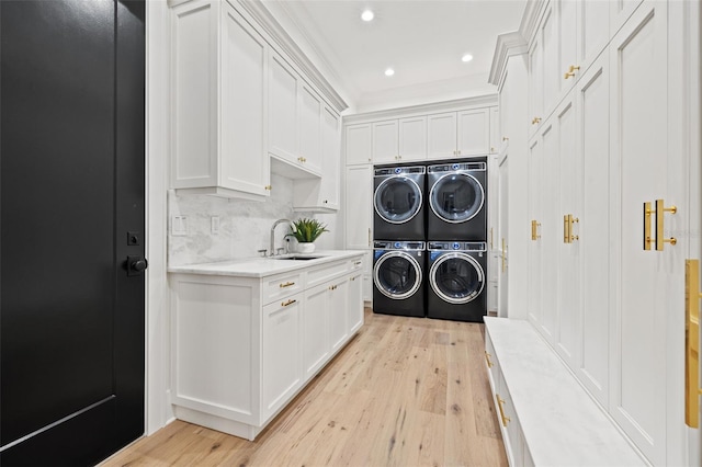 laundry room featuring stacked washer and dryer, a sink, washer and dryer, light wood finished floors, and cabinet space
