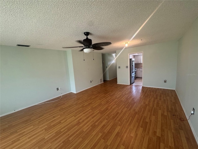 empty room with wood finished floors, baseboards, a ceiling fan, and visible vents