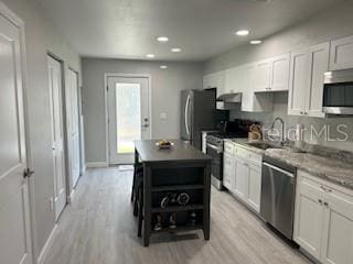 kitchen featuring open shelves, a sink, stainless steel appliances, light wood-style flooring, and a kitchen island
