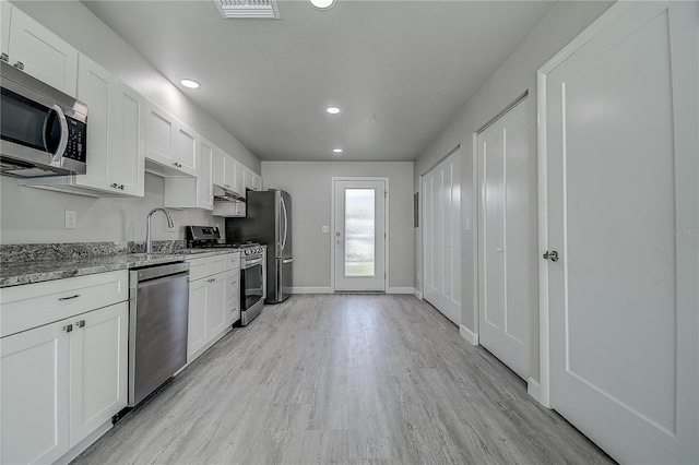 kitchen featuring stone countertops, light wood-type flooring, white cabinetry, appliances with stainless steel finishes, and a sink