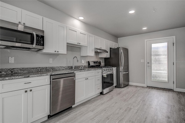 kitchen featuring stone counters, white cabinetry, under cabinet range hood, a sink, and stainless steel appliances