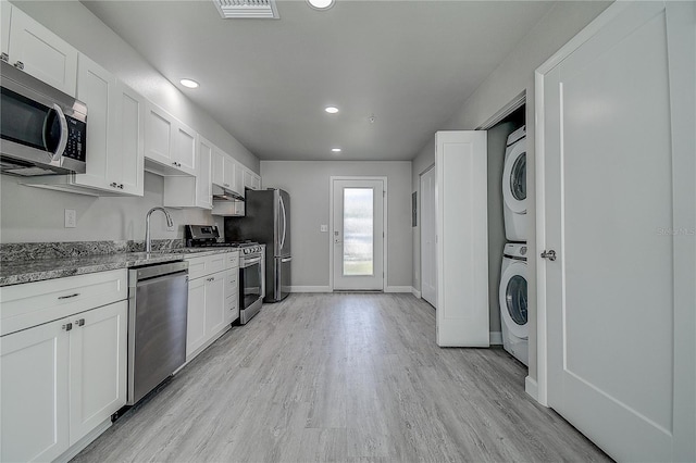 kitchen with stacked washer and dryer, stone counters, a sink, stainless steel appliances, and light wood finished floors