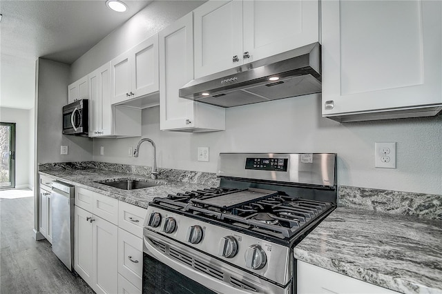 kitchen with light stone countertops, white cabinetry, under cabinet range hood, a sink, and stainless steel appliances