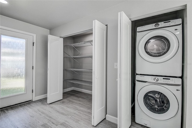 clothes washing area featuring baseboards, stacked washer and clothes dryer, plenty of natural light, and laundry area