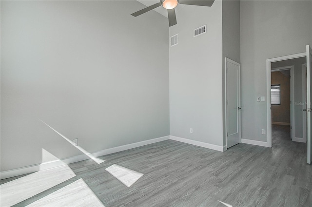 spare room with visible vents, a ceiling fan, a high ceiling, and wood finished floors
