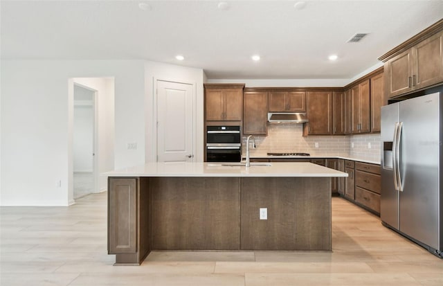 10317 Cross River Trl, Parrish, FL 34219 - kitchen featuring stainless steel appliances, under cabinet range hood, light wood finished floors, an island with sink, and tasteful backsplash
