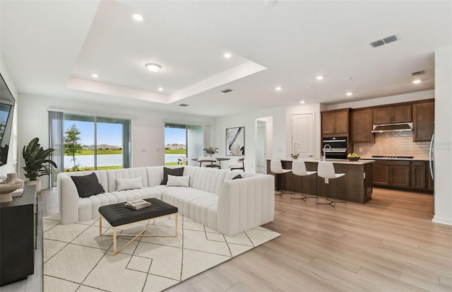 10317 Cross River Trl, Parrish, FL 34219 - living room featuring a tray ceiling, light wood-type flooring, recessed lighting, and a water view