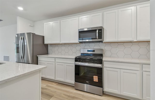 10414 Cross River Trl, Parrish, FL 34219 - kitchen with appliances with stainless steel finishes, white cabinets, decorative backsplash, light wood-style floors, and light stone counters