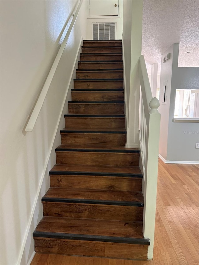 stairway featuring visible vents, baseboards, wood finished floors, and a textured ceiling