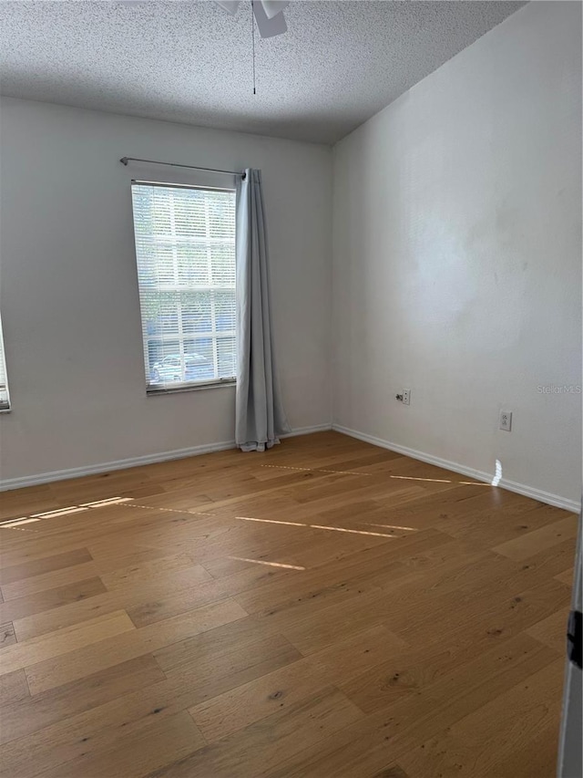 unfurnished room featuring baseboards, a ceiling fan, wood finished floors, and a textured ceiling