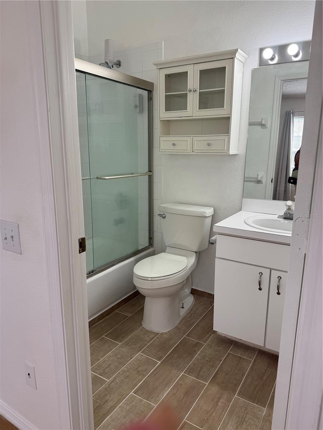 bathroom with wood tiled floor, vanity, bath / shower combo with glass door, baseboards, and toilet
