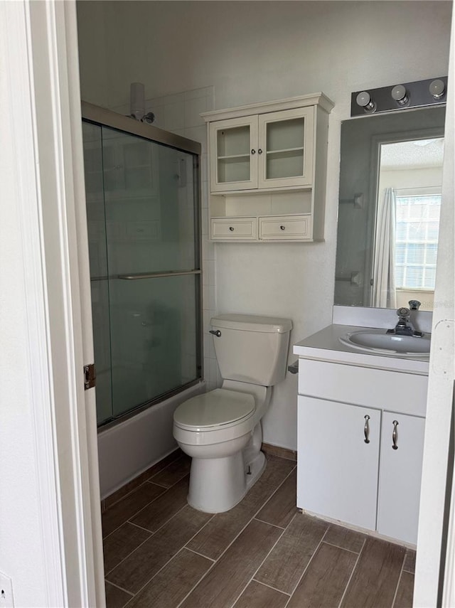 full bathroom with wood finish floors, toilet, vanity, and shower / bath combination with glass door