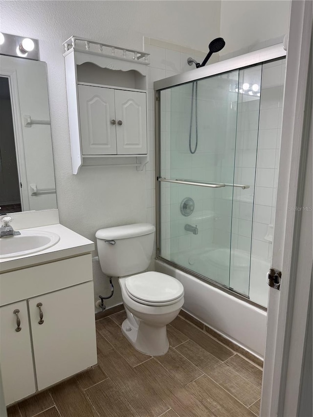 bathroom with wood finish floors, toilet, vanity, and combined bath / shower with glass door