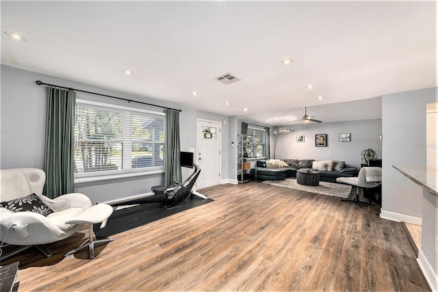 living area featuring baseboards, visible vents, wood finished floors, and ceiling fan