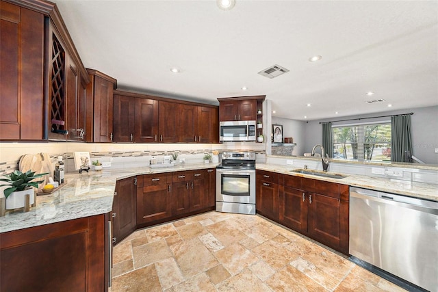 kitchen featuring light stone countertops, a sink, stainless steel appliances, visible vents, and backsplash