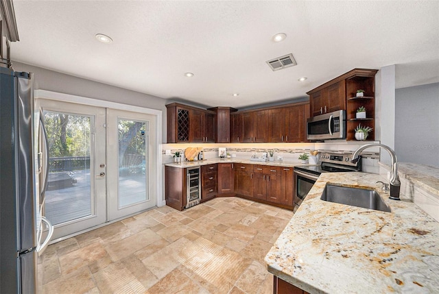kitchen featuring light stone countertops, open shelves, appliances with stainless steel finishes, a sink, and visible vents