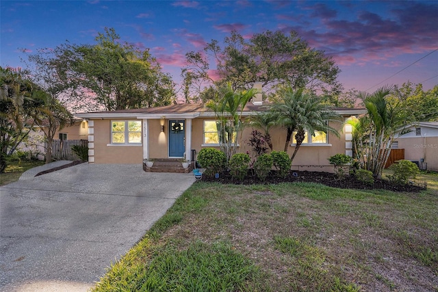 ranch-style home with fence, stucco siding, a front yard, and driveway