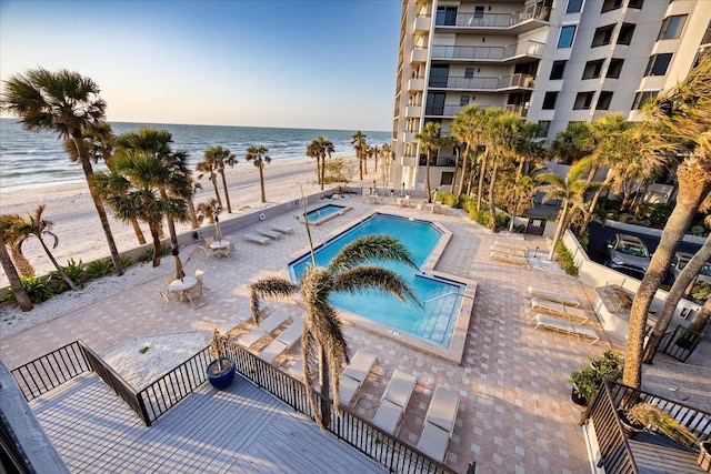 community pool with a view of the beach, a patio, a hot tub, and a water view
