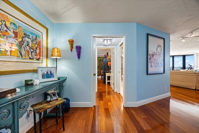 corridor featuring track lighting, baseboards, and wood finished floors