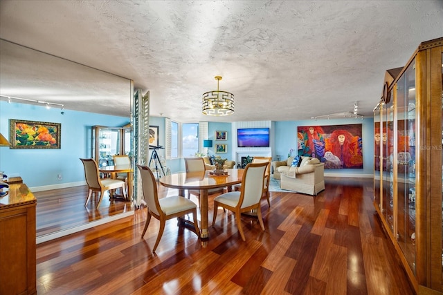 dining room with wood finished floors, an inviting chandelier, baseboards, and rail lighting