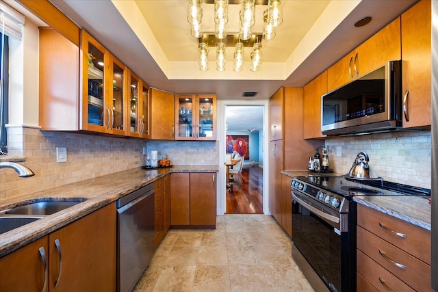 kitchen featuring a raised ceiling, brown cabinets, glass insert cabinets, and stainless steel appliances