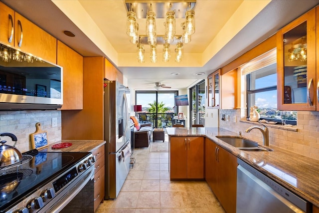kitchen with a peninsula, dark stone countertops, appliances with stainless steel finishes, a sink, and decorative backsplash