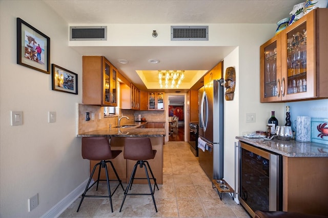 kitchen featuring visible vents, brown cabinetry, freestanding refrigerator, and beverage cooler