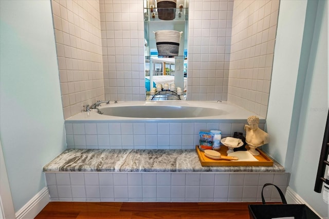 full bath with baseboards, wood finished floors, and tiled tub