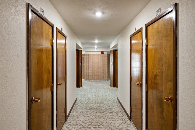 hall with a textured wall and light carpet
