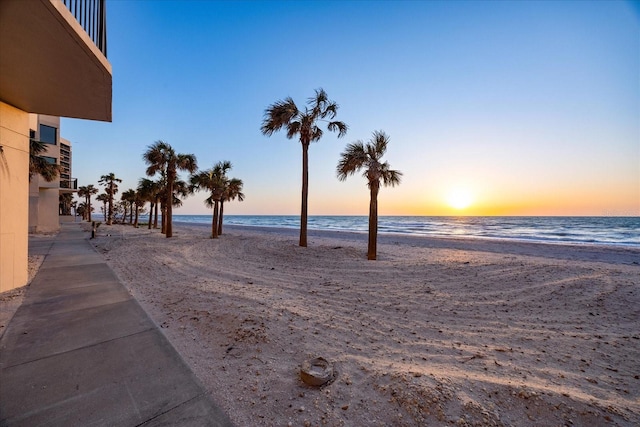 yard at dusk featuring a water view and a view of the beach