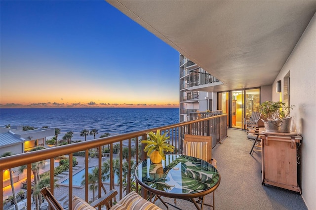 balcony at dusk featuring a water view